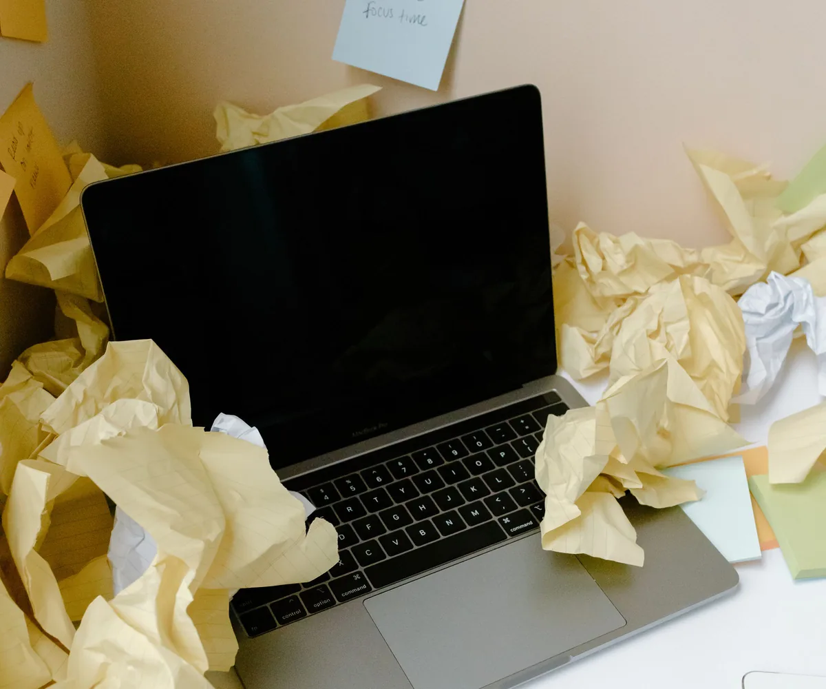 Un laptop sommerso da fogli appallottolati su una scrivania