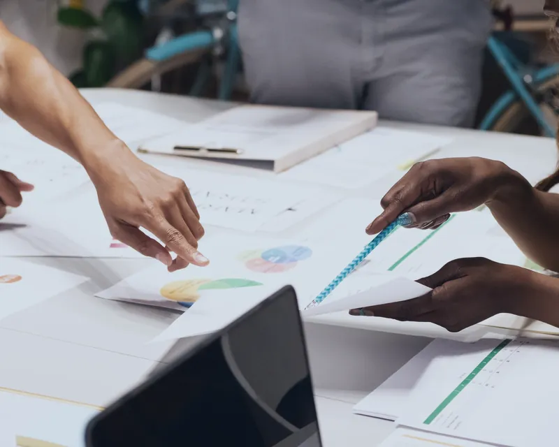 A team pointing at charts and drafts spread on a table