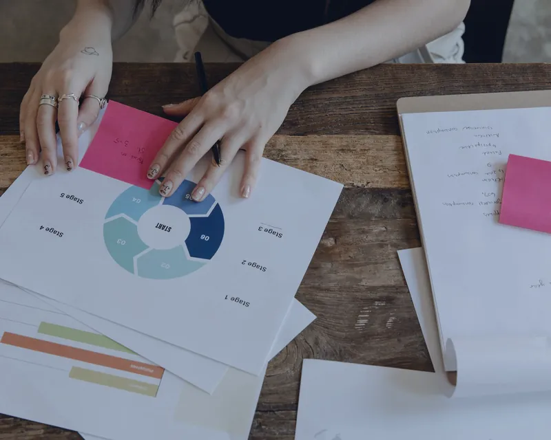 Hands arranging documents, charts and sticky notes on a desk